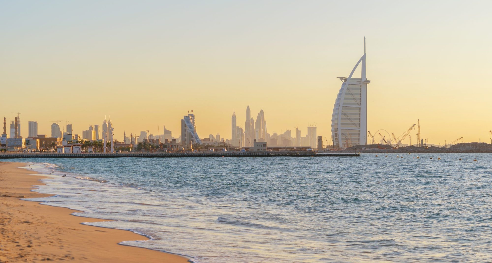 Burj Al Arab in Jumeirah Island or boat building with waves on sea beach, Dubai Downtown skyline, United Arab Emirates or UAE. Financial district in urban city. Skyscrapers at sunset.