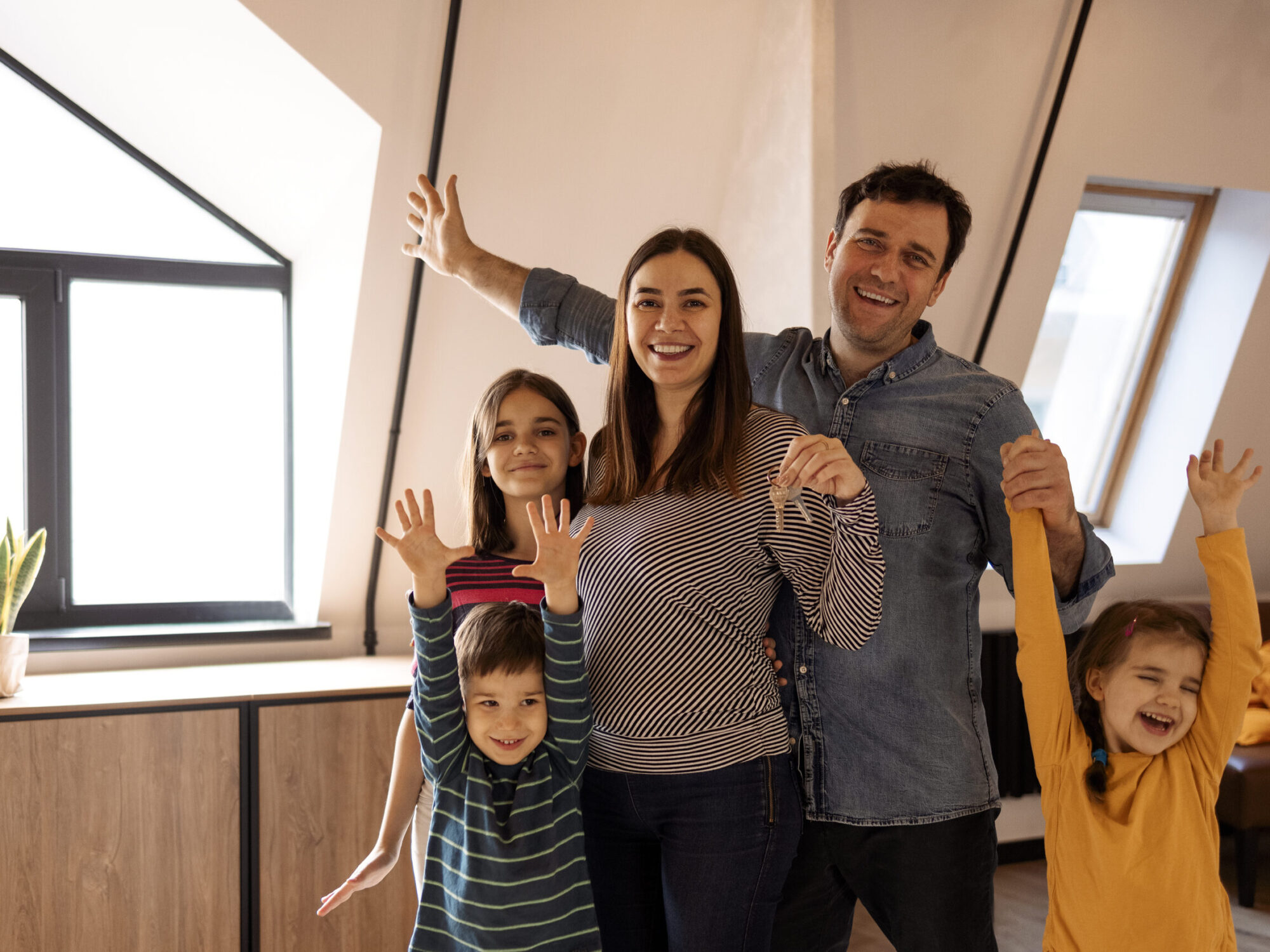 House Ownership. Portrait Of Happy Young family Holding Showing Key Standing In New Flat, Cheerful couple with kids Posing Hugging After Moving to Apartment. Insurance, Real Estate, Mortgage Concept